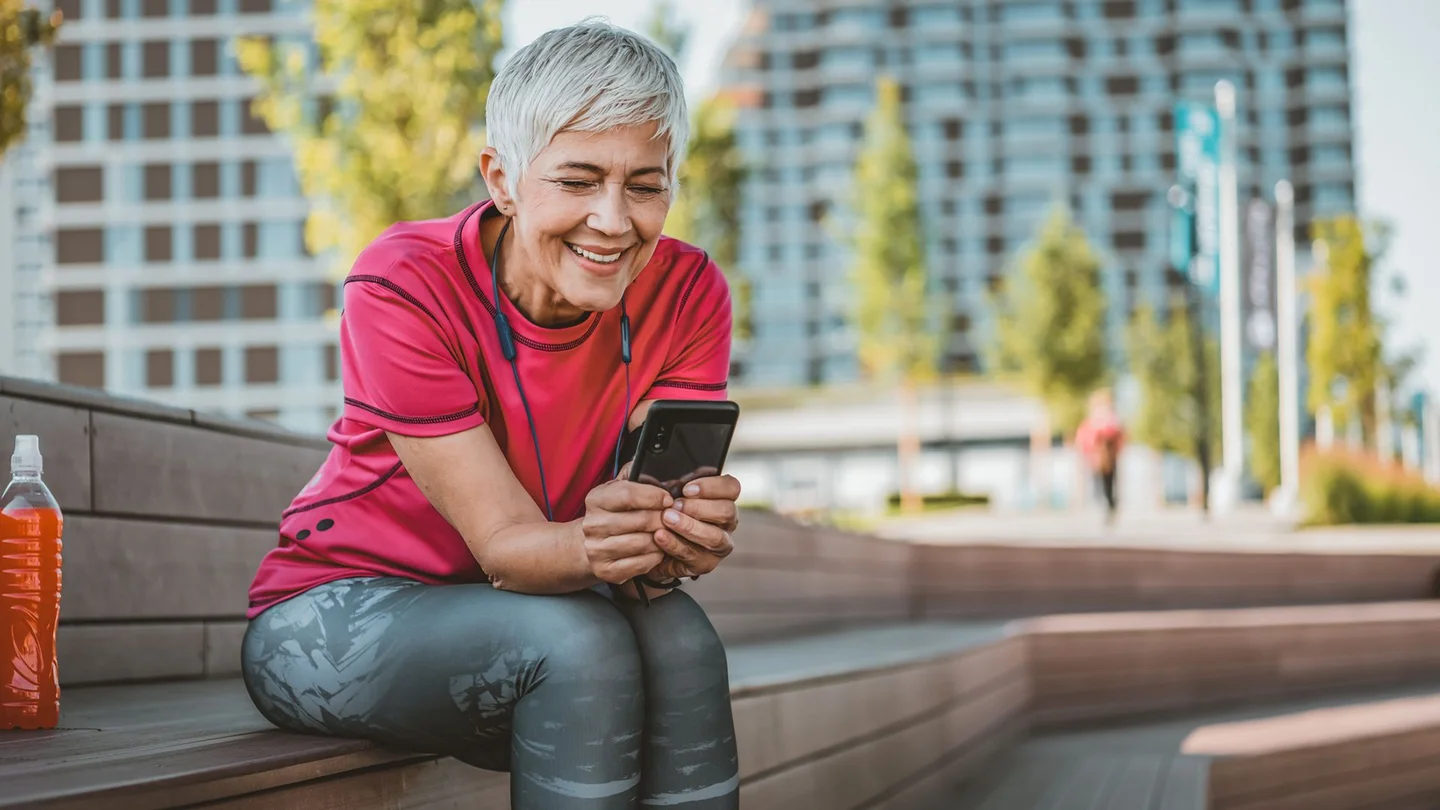 Eine Frau sitzt auf einer Holzbank und schaut auf ein Smartphone.