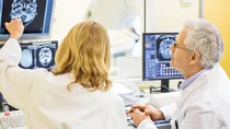 Epilepsie: Eine Ärztin und ein Arzt begutachten das gescannte Bild eines Schädels und Gehirns auf einem Monitor.