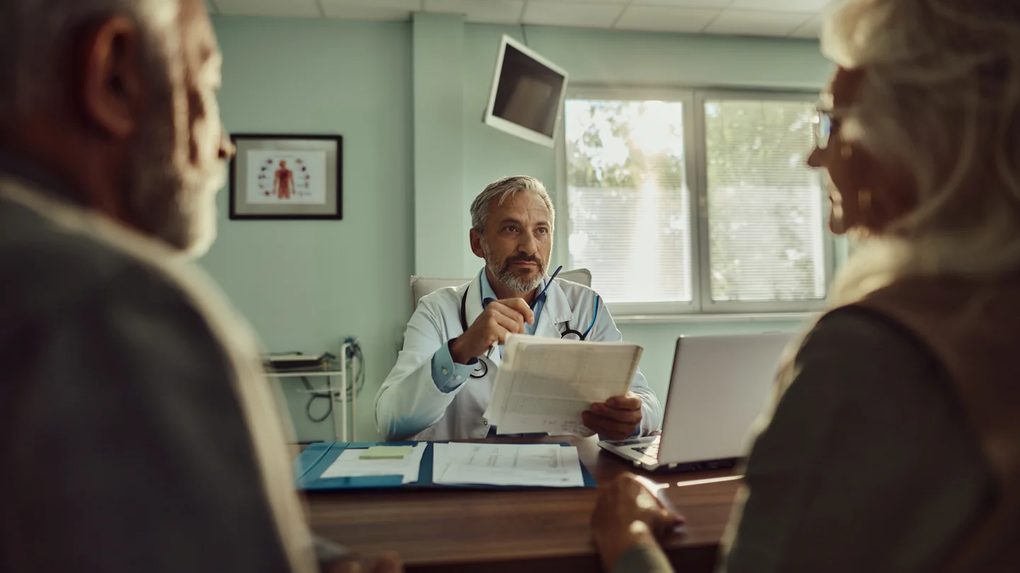 Mann und Frau im Gespr&auml;ch mit einem Arzt im Arztzimmer. 
