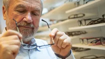 Alterssichtigkeit: Ein älterer Mann begutachtet eine Brille, die er in seinen Händen hält.