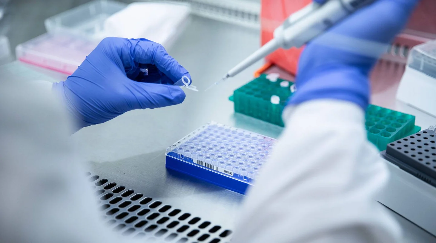 Laborarbeit: Person in Schutzkleidung und Handschuhen mit Pipette und Probenr&ouml;hrchen