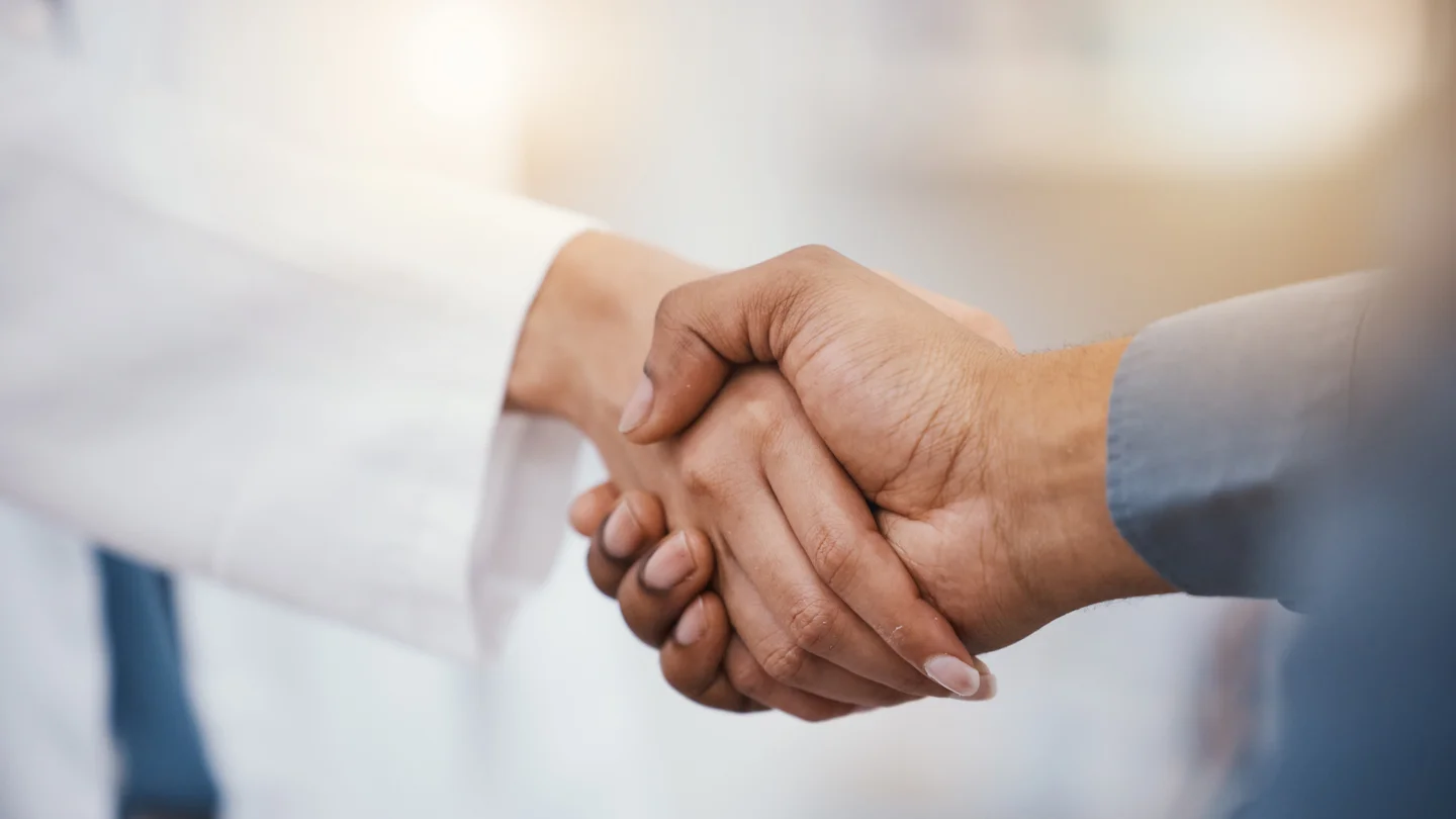 Verbindlicher Händedruck zwischen einer Person im Kittel und einer Person im Hemd.