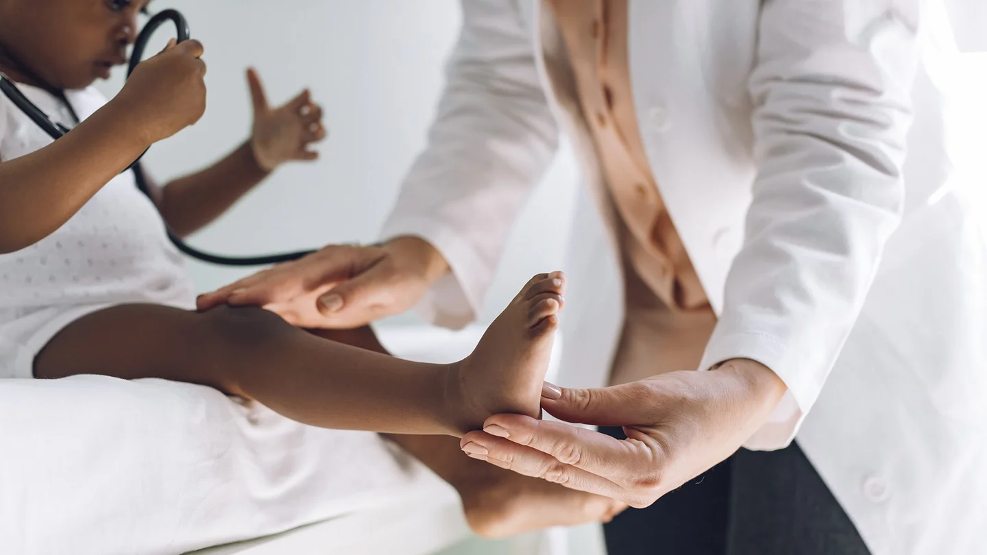 Gesundheitsuntersuchungen f&uuml;r Kinder und Jugendliche: Ein kleines Kind sitzt auf einer Arztliege und spielt mit einem Stethoskop. Eine &Auml;rztin untersucht das Kind vorsichtig.