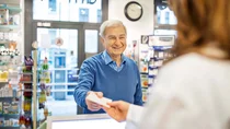 Mann reicht Apothekerin ein Rezept.