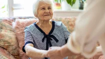 Einer Seniorin wird bei dem Aufstehen von einem Sofa geholfen.