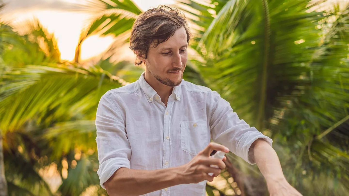 Junger Mann spr&uuml;ht M&uuml;ckenspray auf den Unterarm.