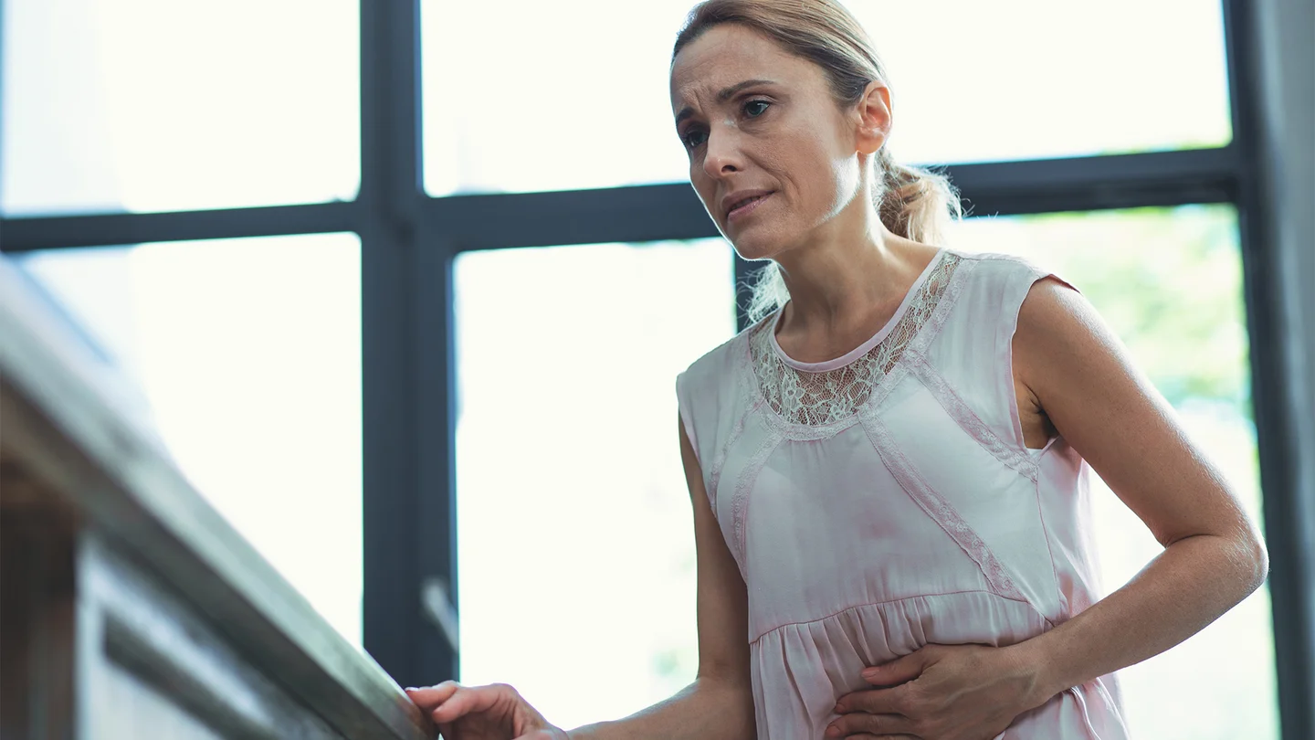 Magengeschw&uuml;r: Eine Frau steht in ihrer Wohnung und h&auml;lt sich den Bauch. Sie wirkt angespannt und als h&auml;tte sie Schmerzen.