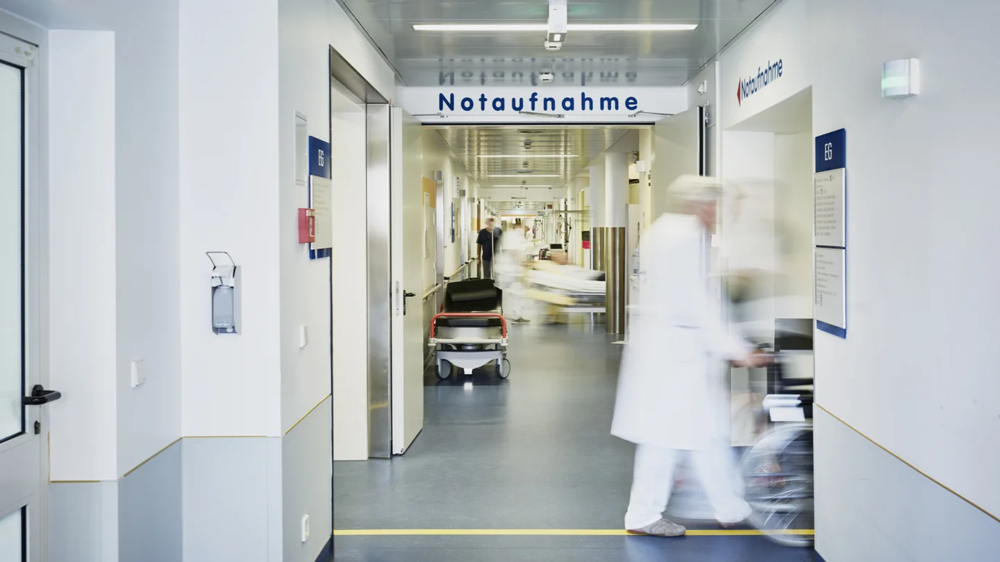 Krankenhauspersonal schiebt einen Patienten im Rollstuhl &uuml;ber den Gang der Notaufnahme