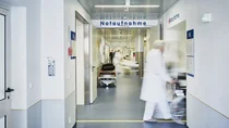 Krankenhauspersonal schiebt einen Patienten im Rollstuhl &uuml;ber den Gang der Notaufnahme